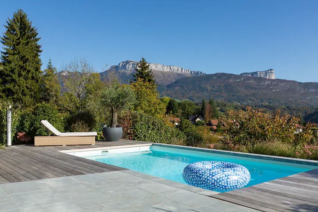 Outdoor pool with inflatable ring, lounge chair, and mountain view under a clear blue sky.
